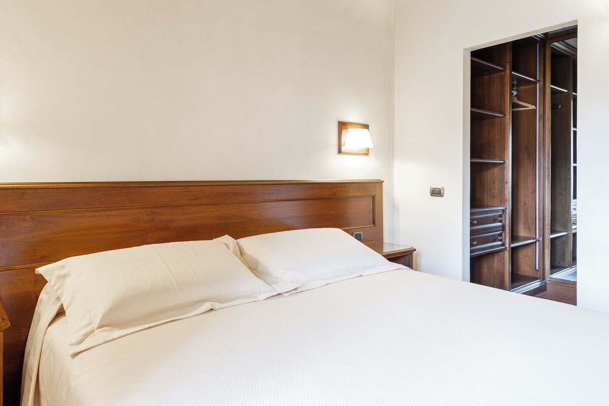 A neatly made bed with a wooden headboard, a bedside table, and a wardrobe with multiple shelves.