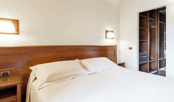 Uma cama bem arrumada com cabeceira de madeira, mesa de cabeceira e guarda-roupa com várias prateleiras.