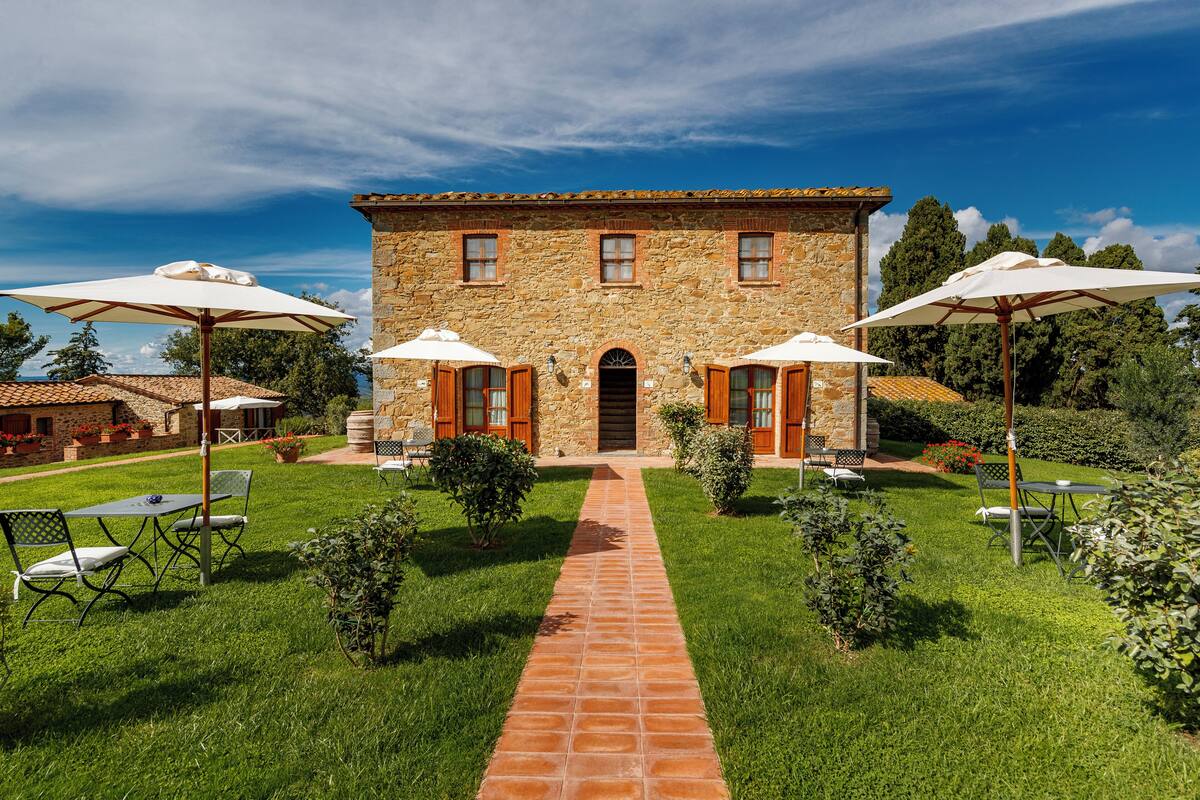 A stone building with a central entrance, surrounded by a well-maintained garden and outdoor seating area.