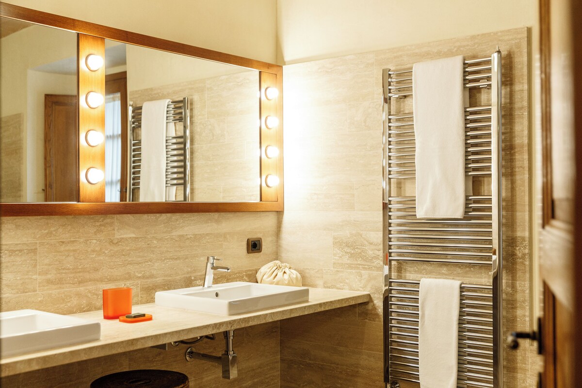 A bathroom with a mirror, two sinks, a towel rack, and a lighted vanity.