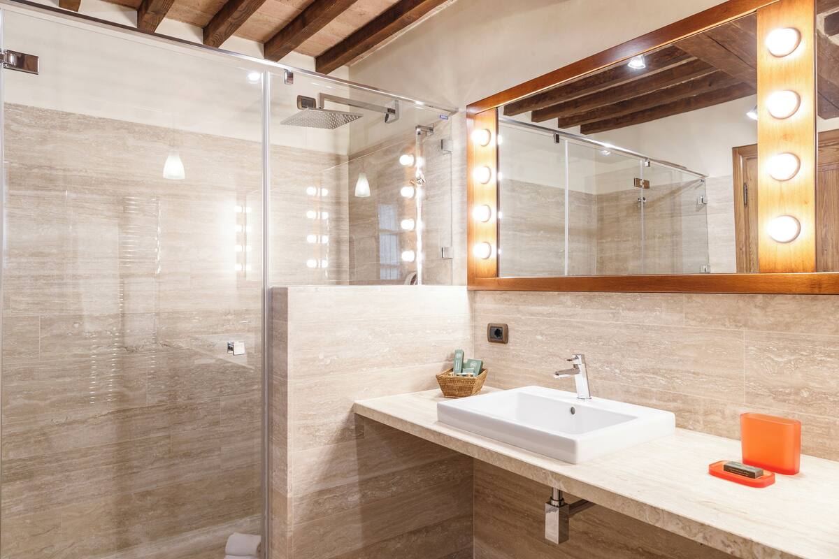 A bathroom with a large mirror, vanity, sink, and shower.