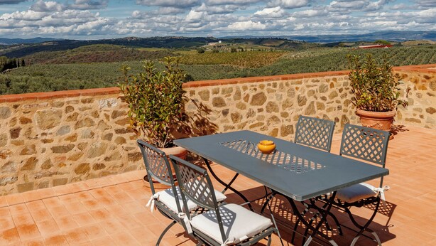 A terrace with a table and chairs, potted plants, and a stone wall. - Tenuta Montecucco (Cinigiano)