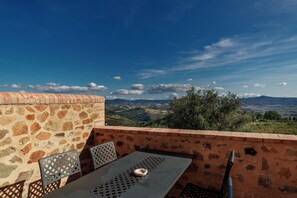 A terrace with a table and chairs, overlooking a scenic landscape with hills and trees. - Tenuta Montecucco (Cinigiano)