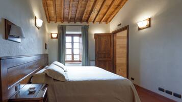 A bedroom with a wooden ceiling, a bed with white linens, a nightstand, a window with curtains, and a wooden wardrobe.