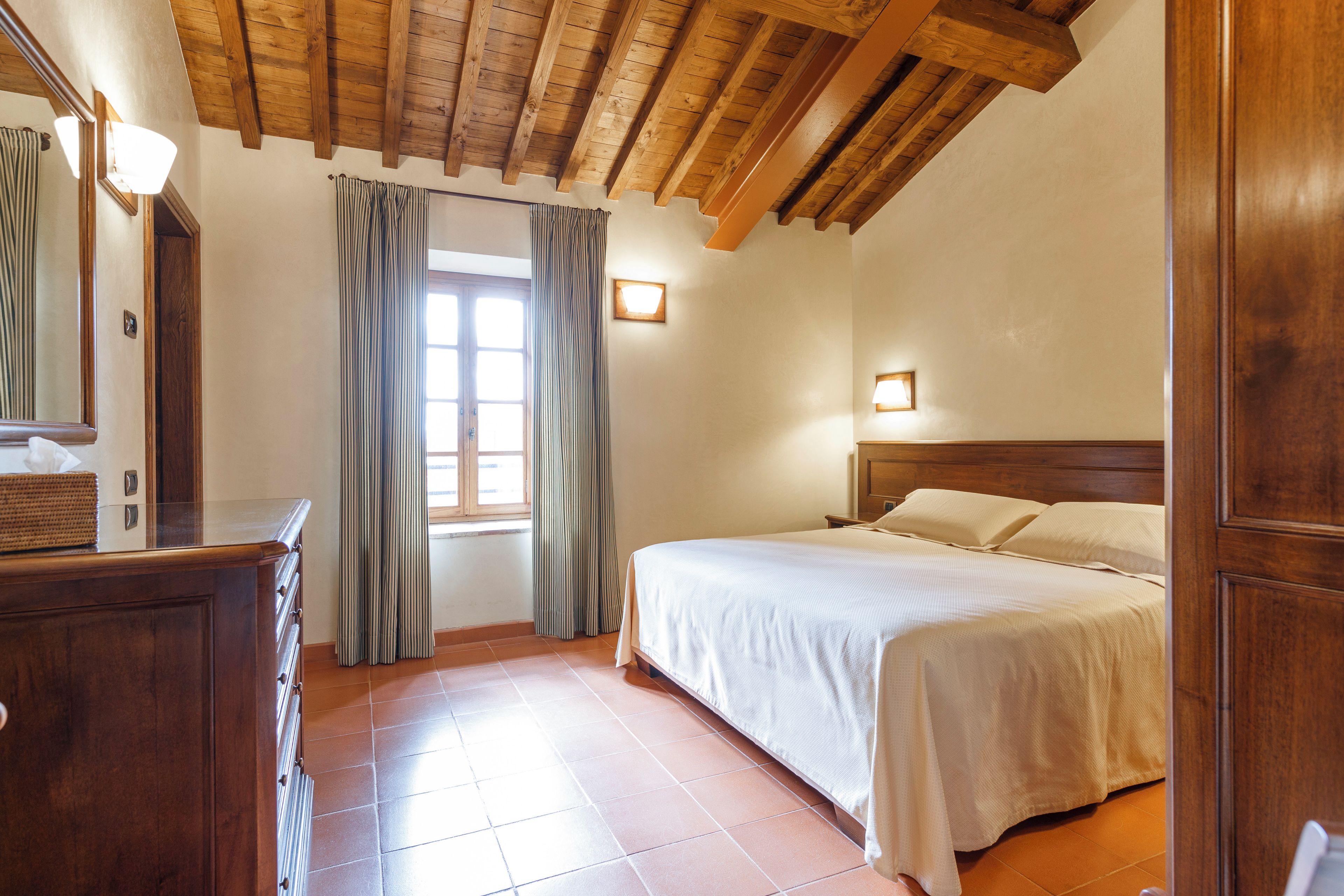 Une chambre avec un plafond en bois, un lit, une commode et une fenêtre avec des rideaux.