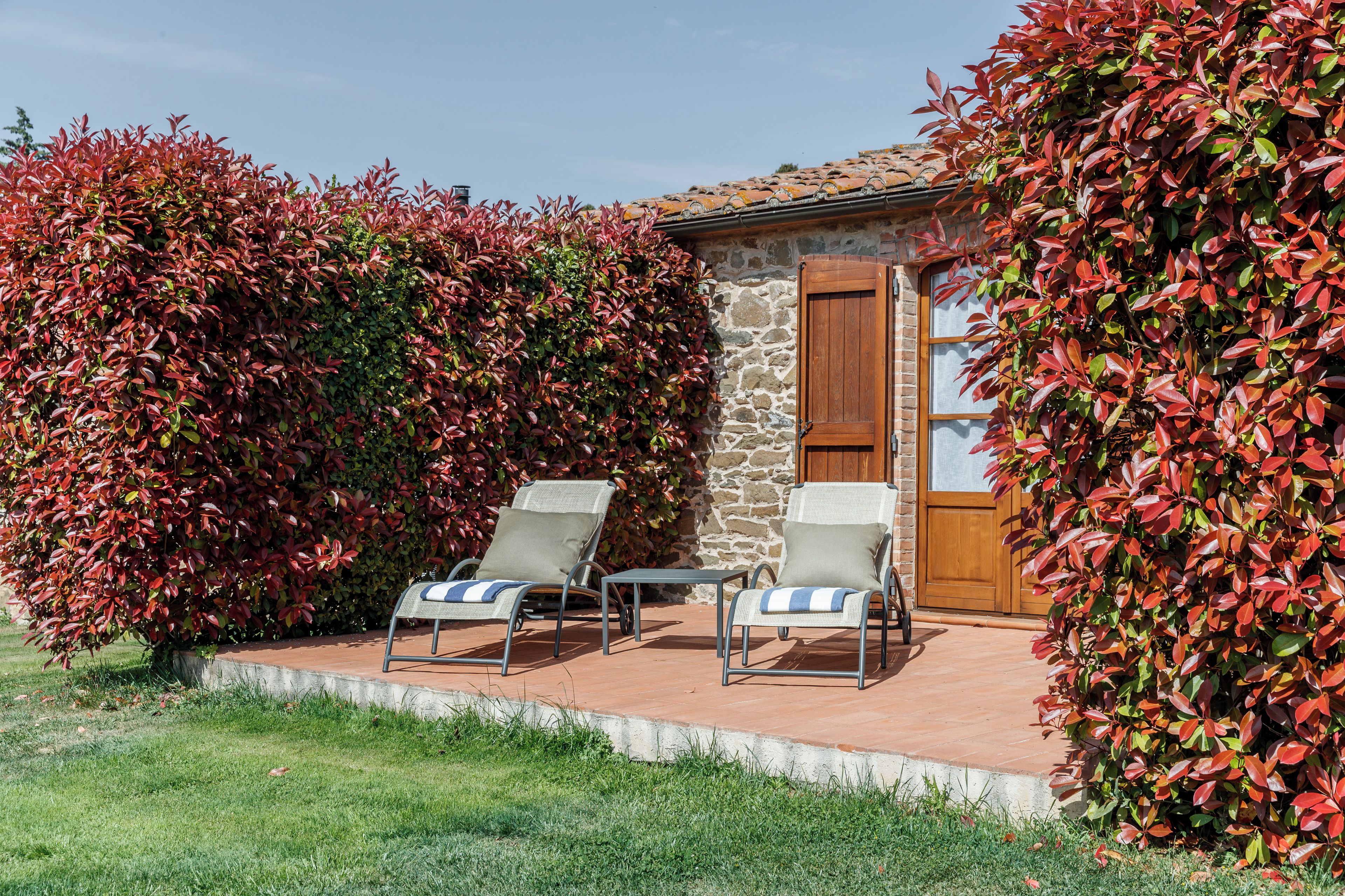 A patio area with two lounge chairs and a small table, surrounded by a stone wall and a wooden door.