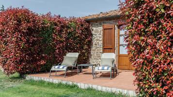 A patio area with two lounge chairs and a small table, surrounded by a stone wall and a wooden door.