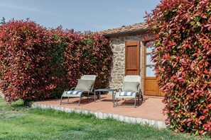 A patio area with two lounge chairs and a small table, surrounded by a stone wall and a wooden door. - Tenuta Montecucco (Cinigiano)