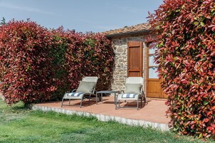 A patio area with two lounge chairs and a small table, surrounded by a stone wall and a wooden door.