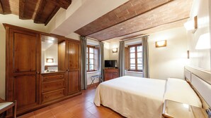 A bedroom with a large bed, wooden wardrobe, and a television. - Tenuta Montecucco (Cinigiano)