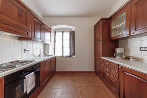 A kitchen with wooden cabinets, a white countertop, and a tiled floor. - Tenuta Montecucco (Cinigiano)