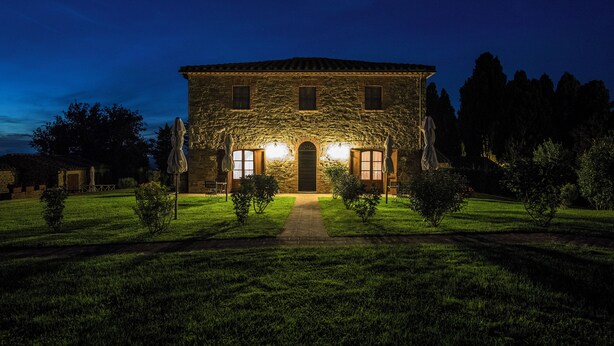 A stone building with a central entrance, surrounded by a well-maintained lawn and trees. - Tenuta Montecucco (Cinigiano)