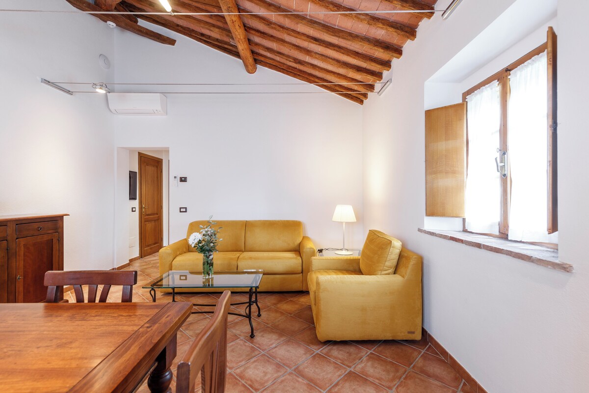 A living room with a wooden ceiling, a yellow sofa, a glass coffee table, and a lamp.