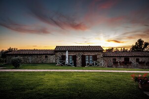 A stone building with a tiled roof, a grassy lawn, and a sunset in the background.