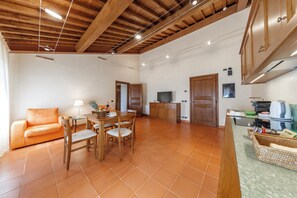 A spacious living area with a wooden ceiling, a dining table with chairs, a sofa, and a kitchen area with cabinets and appliances. - Tenuta Montecucco (Cinigiano)