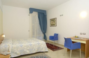 A bedroom with a bed, a desk, two chairs, a window with curtains, and a wall-mounted light fixture. - Residence Rosmari (Brenzone sul Garda)