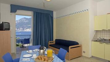 A room with a dining table set for breakfast, a sofa, a kitchen area, and a view of mountains.