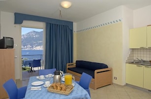 Una habitación con una mesa de comedor dispuesta para el desayuno, un sofá, una zona de cocina y vistas a montañas.
