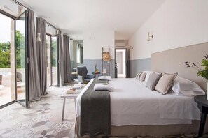 A hotel room with a large bed, a desk, and a view through the glass doors. - Masseria San Giovanni (Fasano)