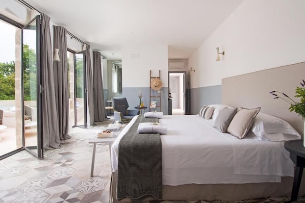 A hotel room with a large bed, a desk, and a view through the glass doors. - Masseria San Giovanni (Fasano)