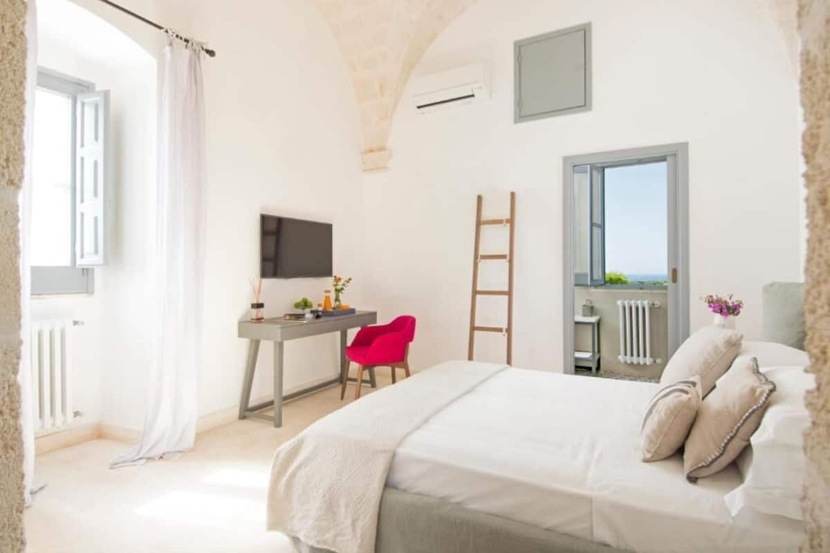 Un dormitorio con cama, escritorio, silla, escalera y ventana con vistas.