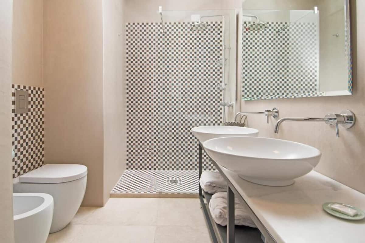 Un baño moderno con pared de ducha a cuadros, un inodoro y dos lavamanos con un espejo encima.