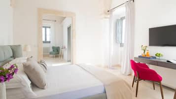 A bedroom with a bed, a desk, a chair, a TV, and a view of another room.