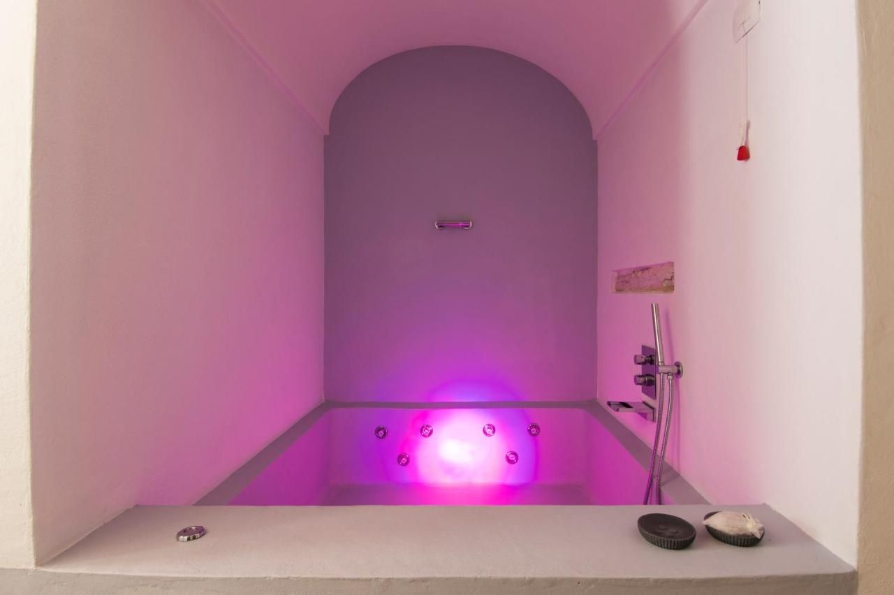 A modern bathroom with a purple-lit bathtub, a shower, and a small shelf with items.