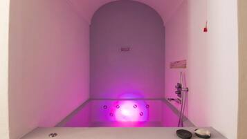A modern bathroom with a purple-lit bathtub, a shower, and a small shelf with items.