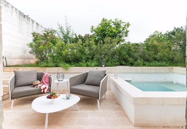 An outdoor seating area with a pool, featuring a sofa, a small table, and a glass.