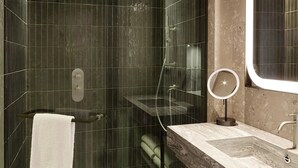 Un bany modern amb dutxa d'ús de vidre, un tocador de marbre i un mirall rodó.