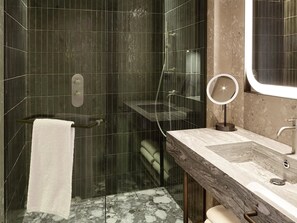 A modern bathroom with a glass-enclosed shower, a marble vanity, and a round mirror. - Hyatt Regency Rome Central (Rome)