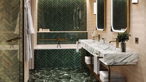 A modern bathroom with a herringbone-patterned green wall, a glass-enclosed shower, a marble vanity, and a large mirror. - Hyatt Regency Rome Central (Rome)