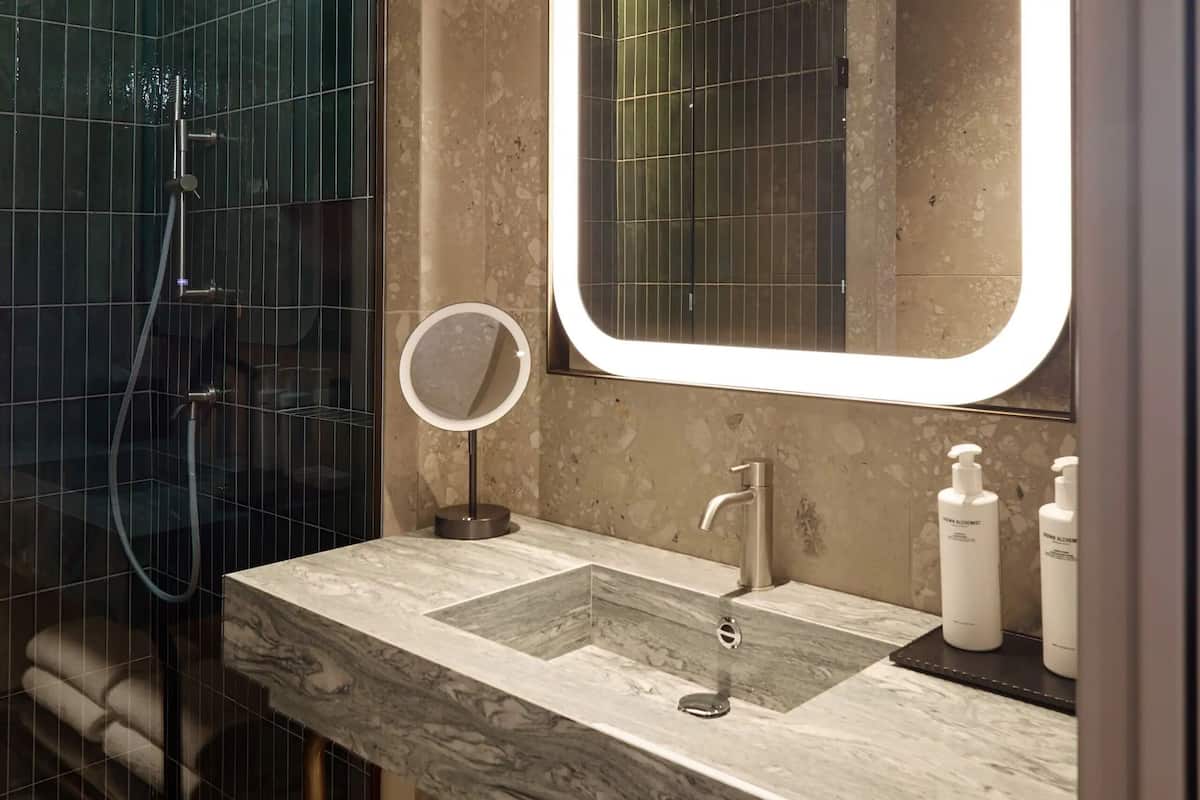 A bathroom with a marble sink, a round mirror, and a handheld showerhead.