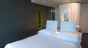 A hotel room with a bed, a bedside table, a mirror, a window with curtains, and a green shelf. - Hyatt Regency Rome Central (Rome)