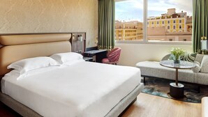 Una habitació d'hotel amb un llit gran, una taula de treball, una cadira i vista a edificis per la finestra.