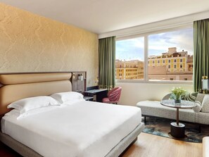Une chambre d’hôtel avec un grand lit, un bureau, une chaise et une vue sur les immeubles par la fenêtre.