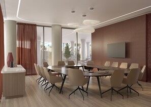 Una sala conferenze moderna con un tavolo rotondo, sedie beige, una TV a parete e ampie finestre che offrono vista su palme.
