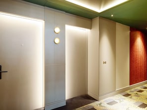 Un corridoio con tappeto decorato, una porta con lampada e un muro con motivo strutturato.