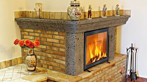 A fireplace with a brick surround and a mantel decorated with figurines and a vase of flowers. - Etna Villa il Pino (Trecastagni)