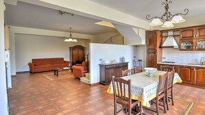 A spacious living area with a sofa, dining table, and chairs, connected to a kitchen with wooden cabinets and a refrigerator. - Etna Villa il Pino (Trecastagni)