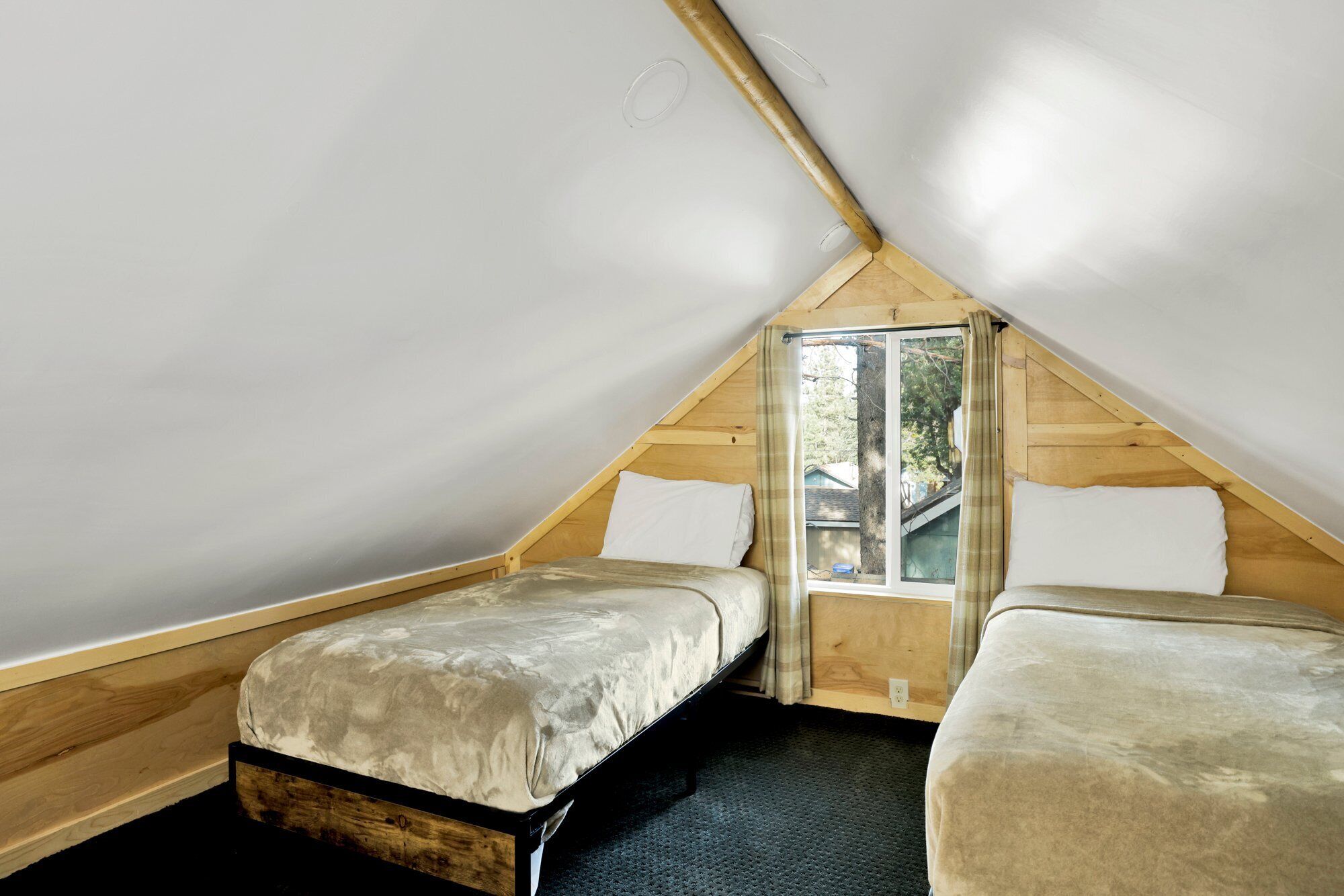 Un pequeño dormitorio en el ático con dos camas individuales, una ventana y paredes de madera.