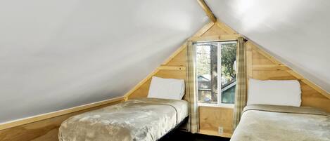 Un pequeño dormitorio en el ático con dos camas individuales, una ventana y paredes de madera.