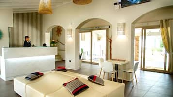 A hotel lobby with a reception desk, a seating area with cushions, and a dining table with chairs.