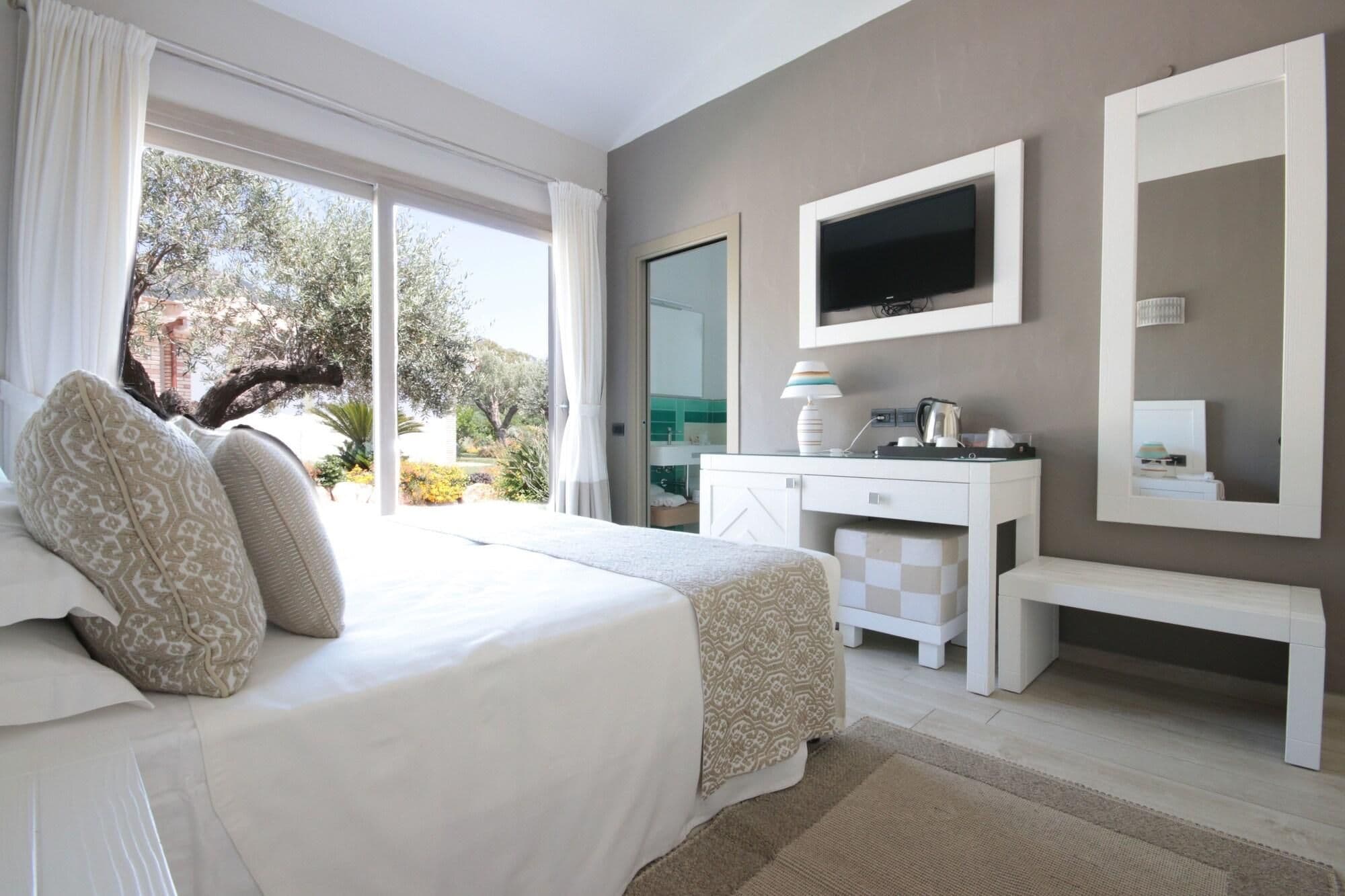 A bedroom with a bed, a desk, a TV, and a large window.