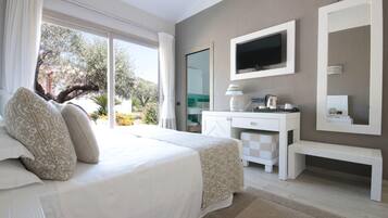 A bedroom with a bed, a desk, a TV, and a large window.