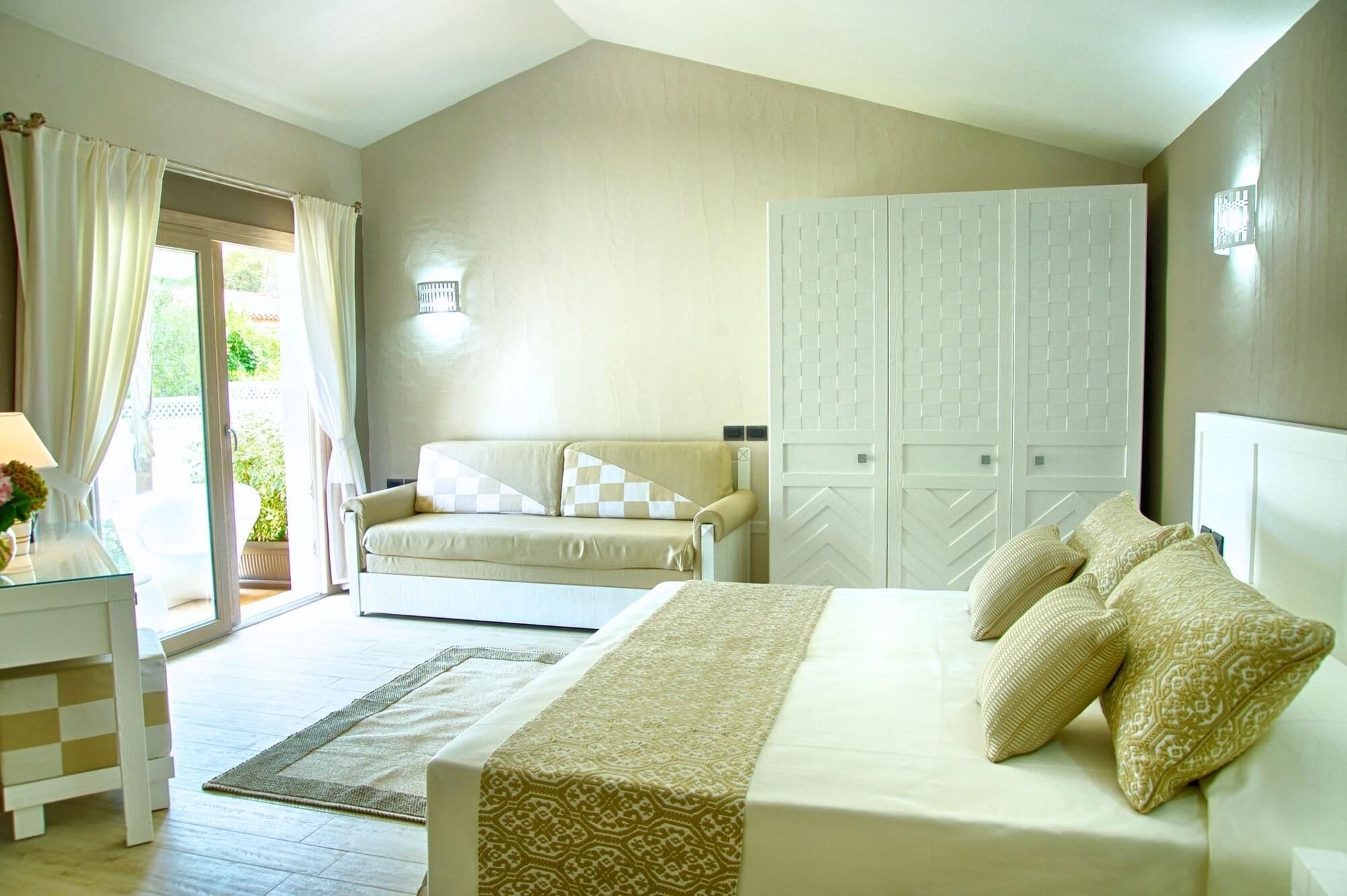 A bedroom with a bed, a sofa, a wardrobe, and a desk with a lamp.