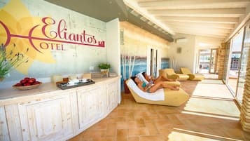 Un lobby moderno de hotel con una recepción, un área de piscina con tumbonas y un amplio ventanal con vistas a la piscina.