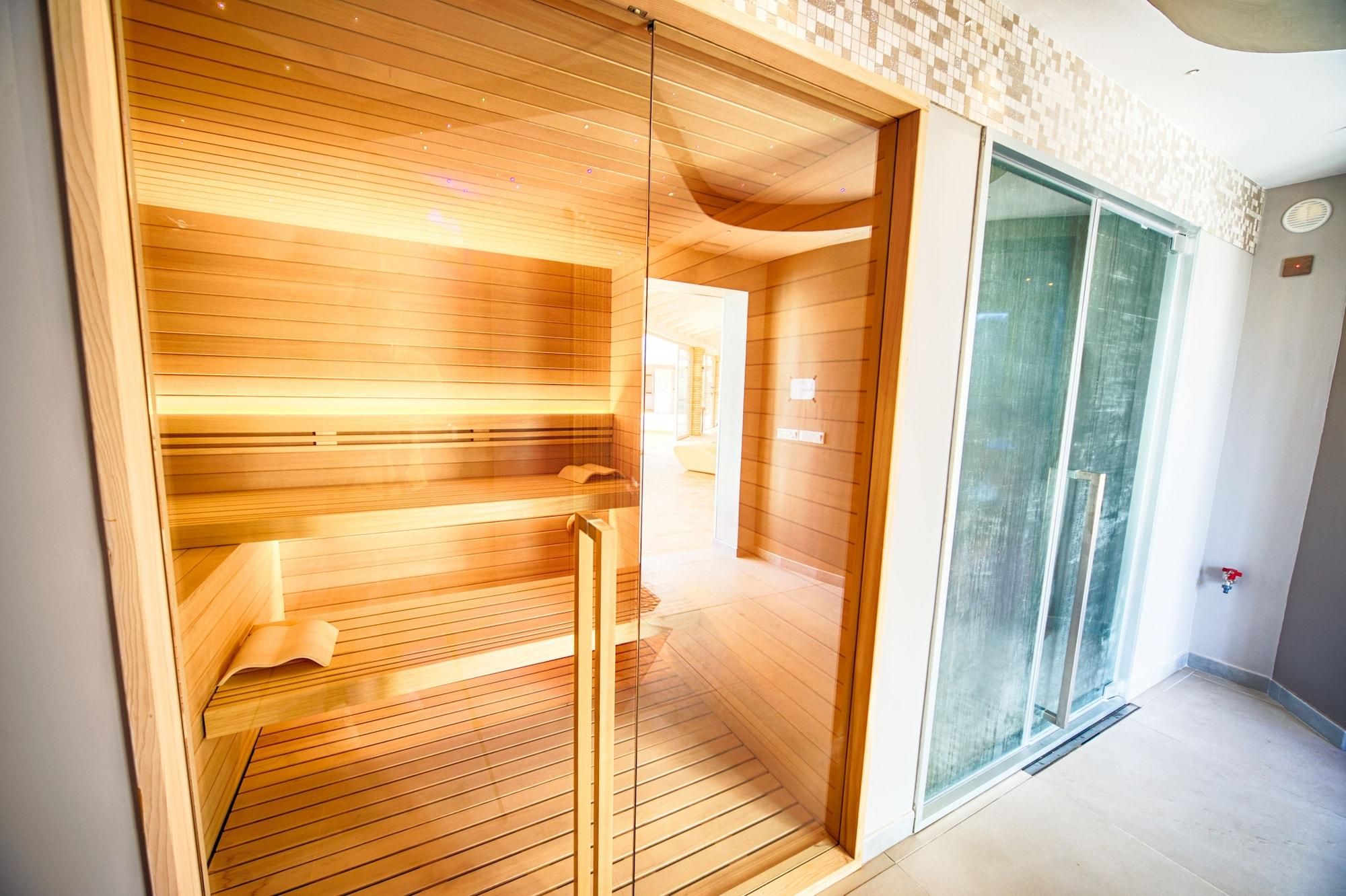 A sauna with wooden benches and glass doors, a tiled floor, and a visible exit door.