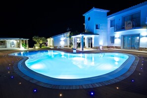 A swimming pool with a wooden deck surrounding it, a building with a balcony, and a well-lit entrance. - Eliantos Hotel and Spa (Pula)